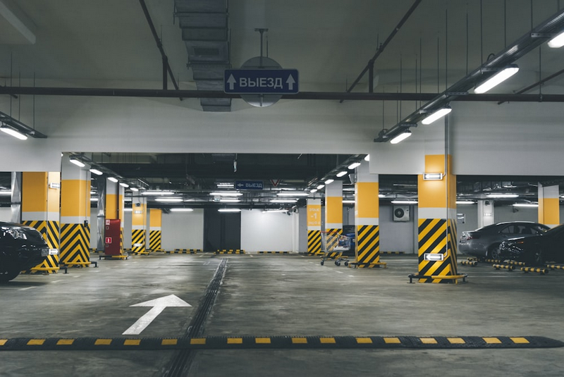 An empty underground parking garage with yellow and black striped pillars and an exit sign.