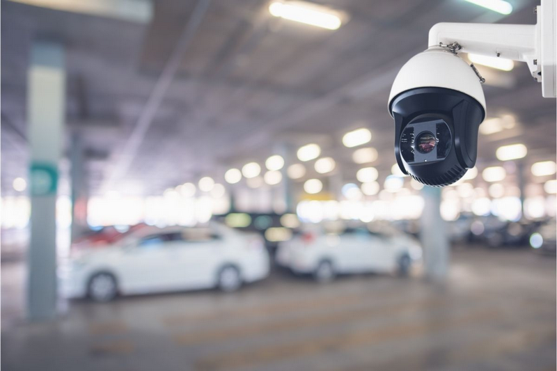 Security camera monitoring a parking garage with several cars.