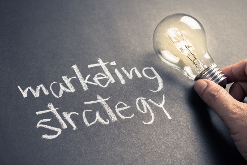 A hand holding a light bulb next to the words marketing strategy written in chalk on a blackboard.