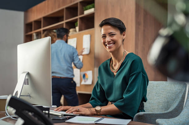 Smiling employee at desk with colleague in background highlights satisfaction linked to accurate payroll management.