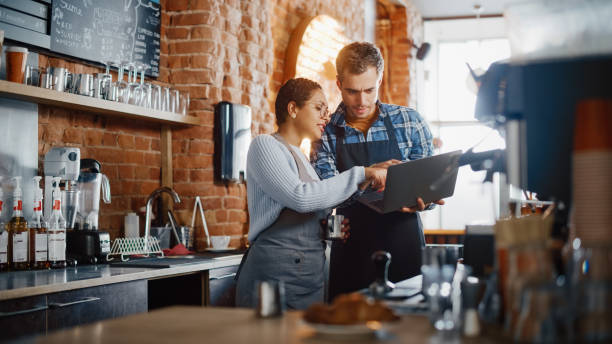 Two small business owners review information on a laptop in their cozy, brick-walled cafe.