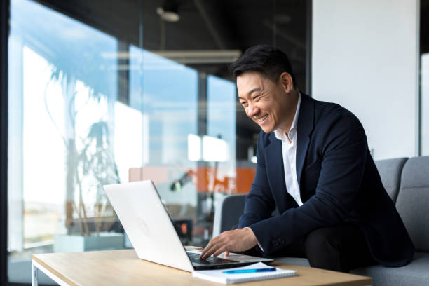 A smiling man in a suit works on his laptop in a modern office, representing small business ownership.